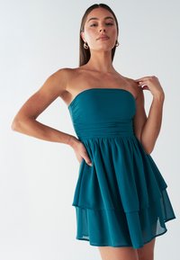 Turboturquoise strapless jurk met geraffineerde lijfje, gelaagde rok en zachte stoftextuur. Beschikt over een aansluitende tailleband en een uitlopende silhouet.