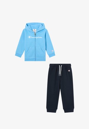 Sudadera con cremallera azul claro con bolsillos, presenta el logotipo en blanco de "Champion" y pantalones de chándal azul oscuro con cordón ajustable y detalles del logotipo.