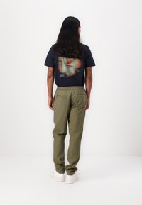 Navyblaues Kurzarm-T-Shirt mit Grafikdruck auf dem Rücken, kombiniert mit olivgrünen, elastischen Hosen und weißen Sneakern.