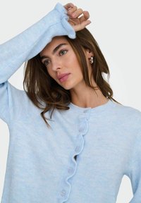 Ljusblå stickad cardigan med rund halsringning, texturerad tyg och en knappplacket med volangkanter längs fram.