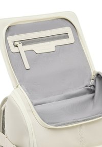 Cremfarbene Rucksackinnenseite mit einem hellgrauen Futter, einer Reißverschlusstasche und glattem Textilmaterial. Minimalistisches Design mit dezentem Branding.