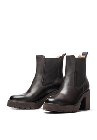 Stivali ankle in pelle marrone con suola spessa e texturata, pannelli laterali elasticizzati e tacco a blocco alto. Design minimalista con dettagli di cucitura.