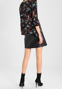Blusa nera a fiori con maniche a tre quarti abbinata a una gonna nera di pelle aderente. Stivaletti con tacco alto completano il look.