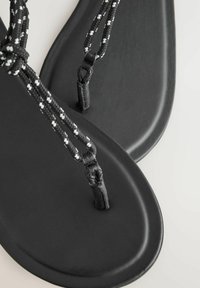 Chanclas negras con suela de goma suave y detalle de tira trenzada en negro y blanco, con un diseño de puntera cerrada y un estilo minimalista.