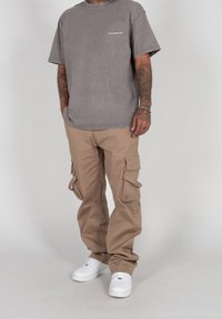 T-shirt oversize grigio chiaro con scollatura rotonda e pantaloni cargo beige con più tasche. Le sneakers bianche completano l'outfit.