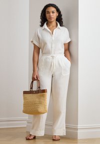 Len overál törtfehér színben, gombos elülső résszel, rövid ujjakkal és húzózsinóros derékkal. Szőtt szalma táska barna fogantyúkkal és díszítésekkel.