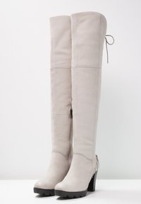 Kozaki za kolano z jasnoszarej skóry z bocznym zamkiem, masywnym czarnym obcasem i ozdobą wiązaną u góry. Gładka faktura, opływowy design.