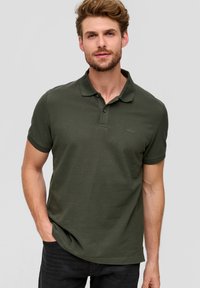 Polo shirt vert foncé en tissu texturé, avec un col classique, une patte de boutonnage et des manches courtes. Détail de logo simple sur la poitrine.