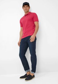 Różowa dopasowana koszulka polo z krótkimi rękawami, niebieskie dżinsy oraz ciemne buty wsuwane. Dżinsy o prostym kroju z podwiniętymi nogawkami.