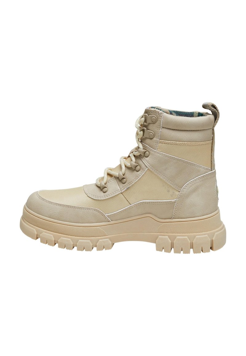 Botas altas beige que presentan una combinación de tela lisa y texturizada, con cordones en la parte delantera y una suela de goma resistente con profundos relieves.