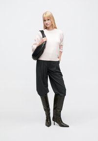 Ροζ ανοιχτόχρωμο πουλόβερ, φαρδιά γραμμή, μανσέτες με ρίγες; μαύροι πλισέ παντελόνες; μαύρα ψηλοτάκουνα μπότες έως το γόνατο; μαύρη τσάντα ώμου. Απλό φόντο.