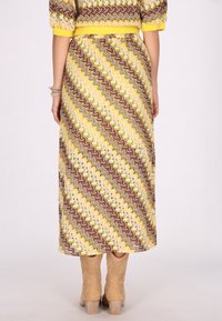 Maxime dress, joka esittelee sahalaitakuosisia ruskean, keltaisen ja vaaleanpunaisen sävyjä. Valmistettu pehmeästä, teksturoidusta kankaasta, jossa on kapeampi vyötärö ja lyhyet hihat.
