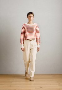 Maglione a strisce rosse e bianche, pantaloni larghi color crema e calzature beige. Design semplice con maniche lunghe e texture a coste.