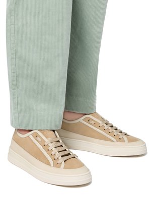 Sneaker beige con pelle liscia e dettagli in suede, suola bianca a contrasto e design classico con lacci. Indossati con pantaloni in corduroy verde chiaro.