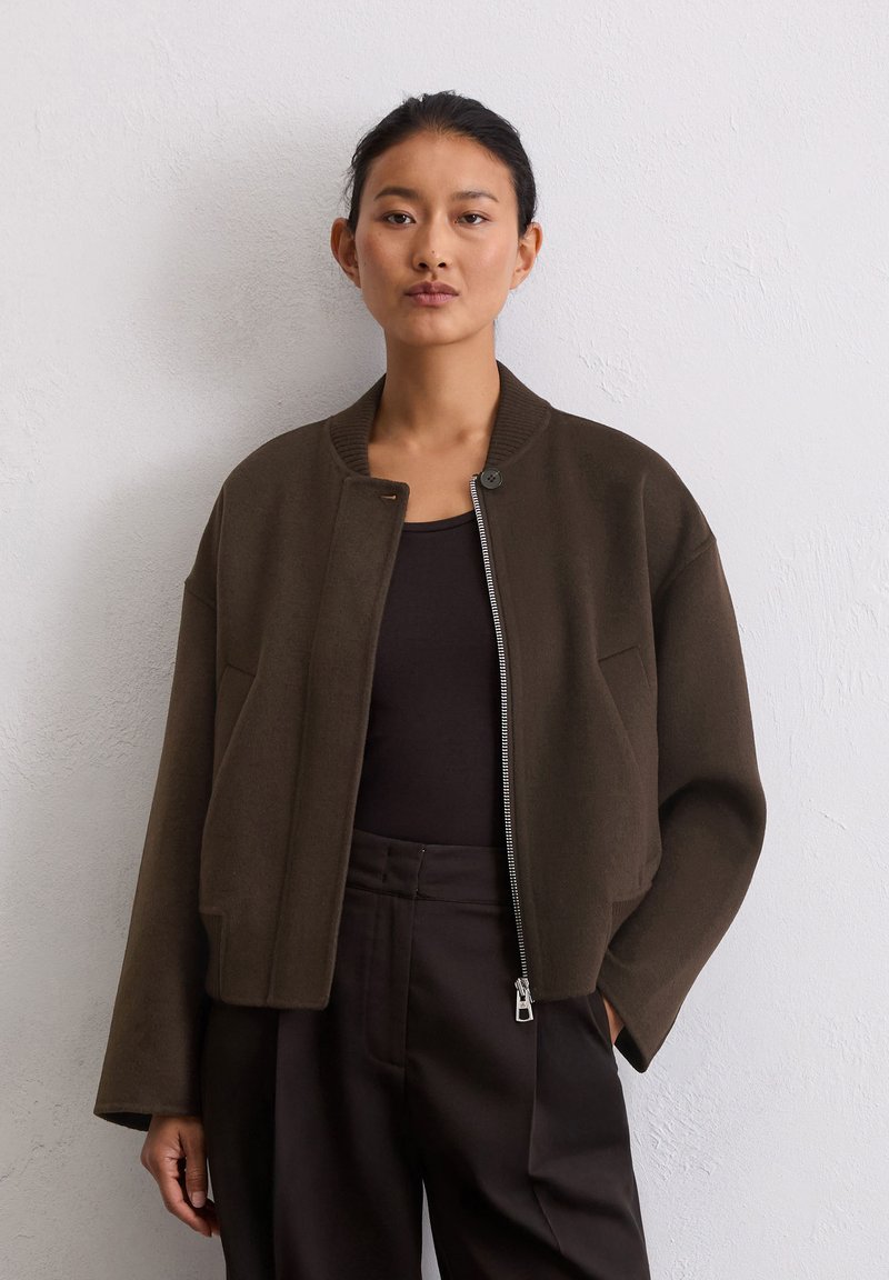 Veste cropped marron avec un col rond, fermeture éclair sur le devant et poches latérales, fabriquée dans un tissu doux au toucher lisse.