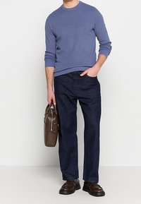 Gebreide blauwe trui met ronde hals, donkere spijkerbroek, bruine leren tas en bruine schoenen. Duidelijke texturen en contrasterende kleuren.