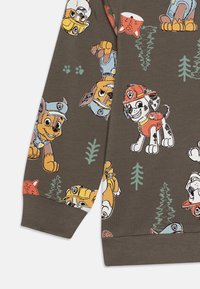 Rjav pulover s karikaturami psov, barvitimi poudarki in drevesi. Tkanina je mehka, z rebrastimi manšetami in sproščenim krojem.