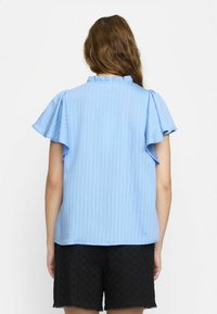 Top azzurro chiaro a maniche corte con scollatura arricciata e righe verticali. Abbinato a pantaloni corti neri, in tessuto testurizzato, con motivi intricati.