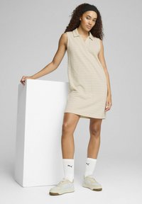 Beige ärmlös polo-klänning med subtila ränder, badad med ljusa sneakers och vita strumpor. Enkel design med en avslappnad passform.