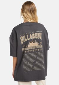 Overdimensioneret sort t-shirt lavet af bomuld, med et grafisk tryk på ryggen, som har tekst og solmotiver i beige og guld accenter.