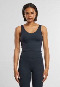 Tmavo šedý bezrukávový crop top s V-výstrihom a hladkou textúrou, skombinovaný s legínami s vysokým pásom, ktoré zvýrazňujú priliehavý športový dizajn.