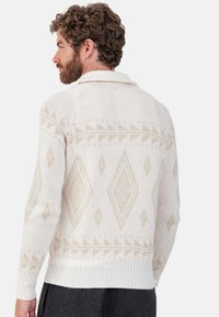 Pull crème avec un col plié, présentant un motif géométrique beige de losanges et triangles, avec des poignets et un ourlet côtelés.