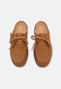 Brown suede slip-on shoes with rounded toe, lace-up design, textured rubber sole, and tan laces. Slightly cushioned insole visible.