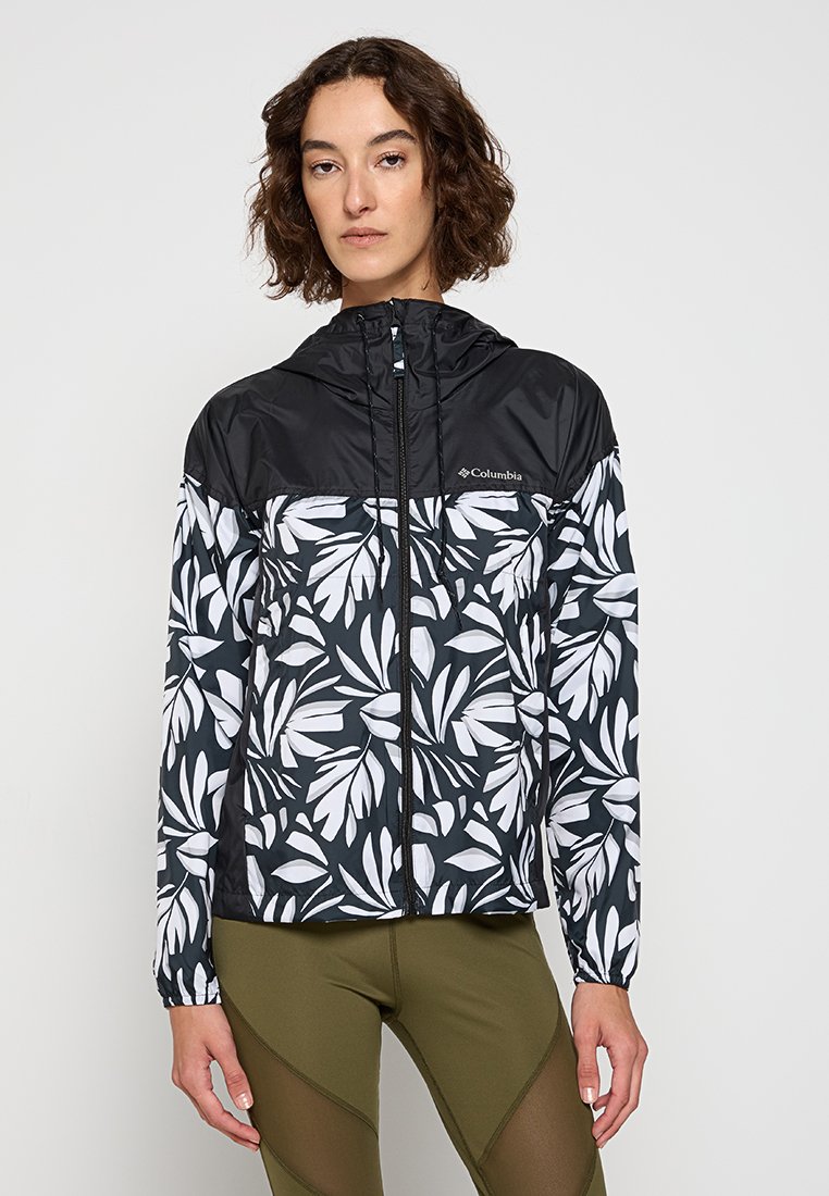 Chaqueta ligera con capucha y estampado floral en blanco y negro, que cuenta con un cierre completo y puños elásticos. Los materiales reflejan un diseño deportivo.