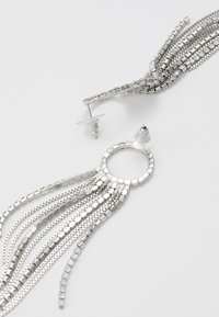 Orecchini in argento con un accento circolare e molte catene a cascata, composte da piccoli anelli quadrati e tondi, che conferiscono un aspetto testurizzato.