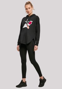 Black hoodie with a graphic of a cartoon character on the front, featuring red accents. Paired with black leggings and athletic shoes.