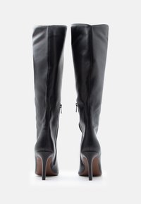 Μαύρες δερμάτινες μπότες έως το γόνατο με στιλέτο τακούνια, διαθέσιμες με φερμουάρ στα πλάγια και λεία υφή.