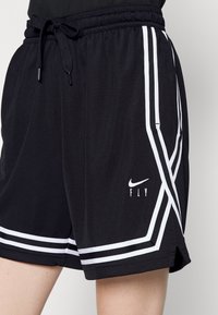 Mustat urheilushortsit, joissa on teksturoitu kangas, valkoiset raidat sivuilla ja pieni Nike-logo, jonka alla lukee "FLY".