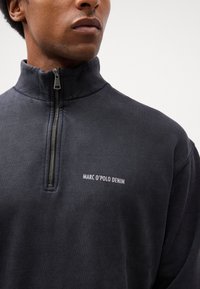 Mørkegrå zip-up sweatshirt med høj krave, lavet af tekstureret stof, med "MARC O'POLO DENIM" logoet i hvidt på brystet.