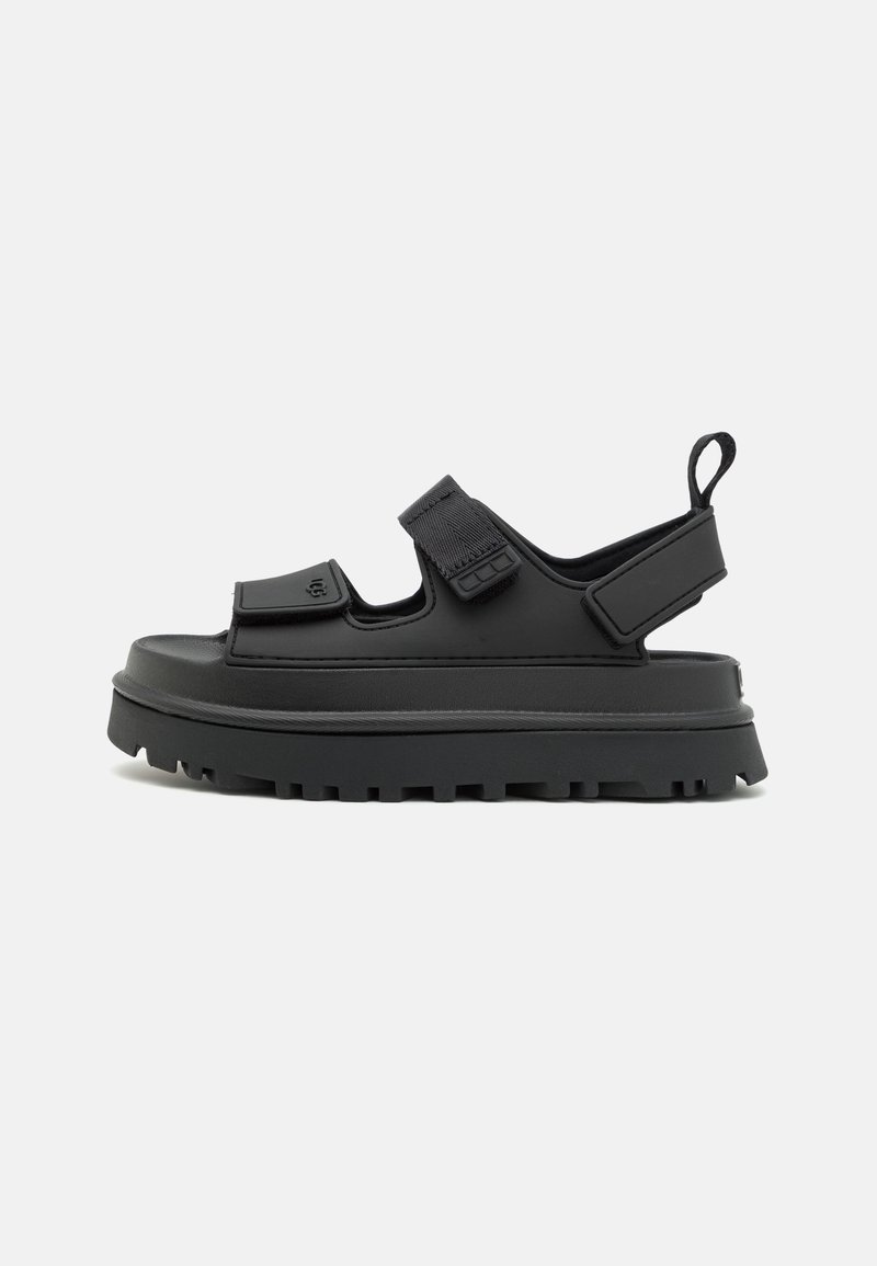 Sandale à plateforme noire avec une semelle épaisse, deux brides Velcro réglables sur le dessus du pied et une autour du talon avec une languette.