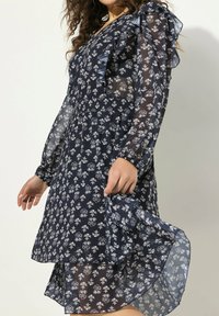 Vestido floral azul marino hecho de un tejido ligero y transparente. Presenta mangas con volantes y una cintura elástica con una falda en capas y fluida.