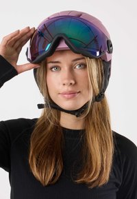 Lila Skihelm mit verspiegeltem Visier, verstellbarem Kinnriemen und Belüftungsöffnungen. Wird von einer Person mit langen Haaren drinnen getragen.