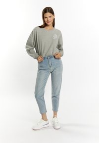 Grijze sweatshirt met een ronde hals en geborduurde details, gecombineerd met lichtblauwe high-waisted jeans en witte sneakers met paarse accenten.