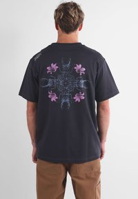 T-shirt noir à manches courtes avec un large graphique de scorpions symétriques et de fleurs roses au dos. Design classique à col rond.