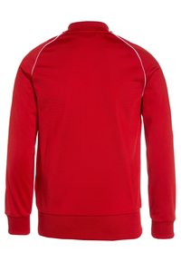 Červená dlouhá mikina s vysokým límcem, se bílými lemy na ramenou, vyrobená z hladkého textilního materiálu.