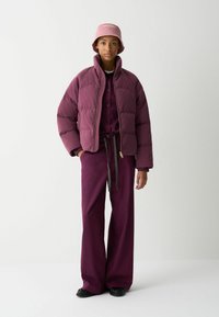 Puffet bordeaux jakke med høj krave, parret med en matchende top og brede bukser. Bucket hat i en lysere nuance af bordeaux.