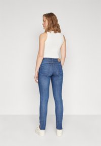 Blå denim skinny jeans med mid høyde liv, med design av baklomme og sidespalter ved ankler, kombinert med en hvit ermeløs topp.