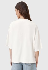 T-shirt oversize bianco, maniche corte, collo rotondo, materiale di cotone morbido, vestibilità rilassata, orlo dritto, senza motivi o dettagli visibili.