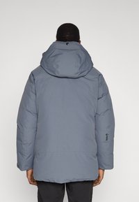 Šedá izolovaná bunda s velkou kapucí a elastickými manžetami. Na levém rukávu je logo a bunda má hladký matný povrch.