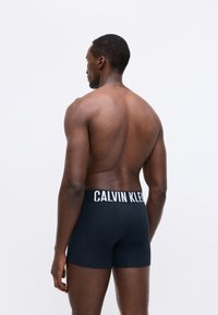 Férfi fekete boxer alsónadrág fehér rugalmas derékkal, rajta a "CALVIN KLEIN" márkázással. Simaság jellemzi, testhezálló kialakítással, látható minták nélkül.