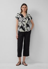 Zwart kortarmig shirt met witte bladerenprint, v-hals ontwerp, gecombineerd met losse zwarte cropped broek en zwarte sandalen.