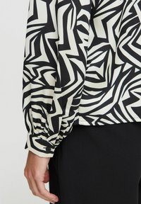 Camicia a maniche lunghe con un motivo astratto in bianco e nero, caratterizzata da polsini arricciati e una texture del tessuto liscia.