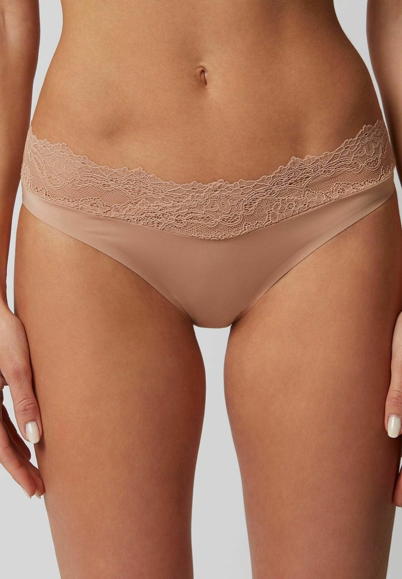 Huidskleurige onderbroek met een bloemenkant tailleband. Zacht materiaal, minimale bedekking, naadloos ontwerp en delicate kantdetails langs de bovenkant.