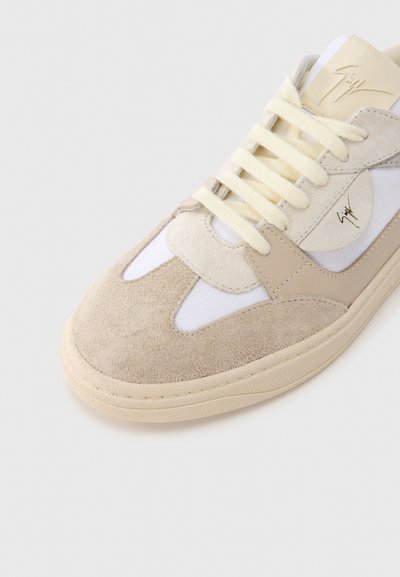 Smėlinės spalvos zomšiniai ir tinklelio sportbačiai su kreminėmis raištelėmis, apvalia nosimi ir kontrastingu rudos spalvos paneliu. Šone auksinis logotipas.