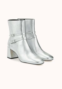 Bottes cheville métalliques argentées avec un bout pointu, un talon bloc et deux sangles réglables sur le devant. Texture lisse et design élégant.