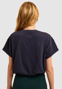 T-shirt bleu marine à manches courtes avec une coupe décontractée et des manches retroussées, fabriqué en coton doux. Design simple et sans ornements au dos.